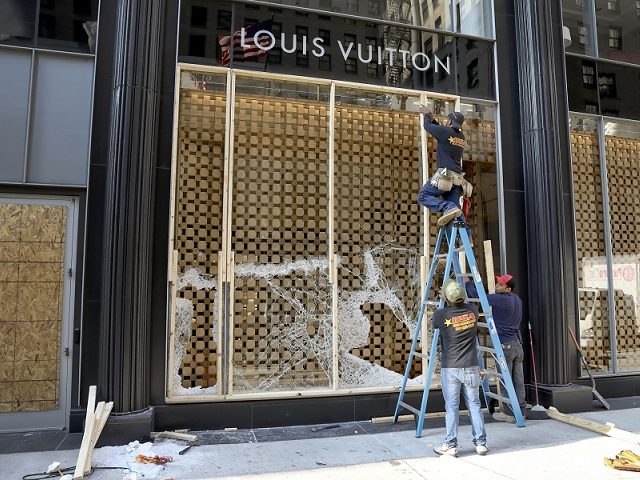 Workers begin to board up a display window at the Louis Vuitton store Monday, Aug. 10, 2020, after overnight vandals hit many high-end stores in Chicago. Chicago's police commissioner says more than 100 people were arrested following a night of looting and unrest that left several officers injured and caused …
