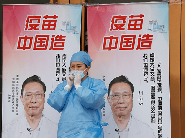 A medical worker adjusts her mask near propaganda boards showing famed Chinese medical expert Zhong Nanshan and the words "Vaccine China Made" outside vaccination center in Beijing Friday, April 9, 2021. In a rare admission of the weakness of Chinese coronavirus vaccines, the country's top disease control official says their effectiveness is low and the government is considering mixing them to give them a boost. (AP Photo/Ng Han Guan)