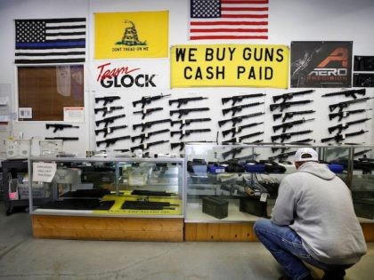 A customer looks at handguns in a case as AR-15 style rifles hang on a wall at Davidson De