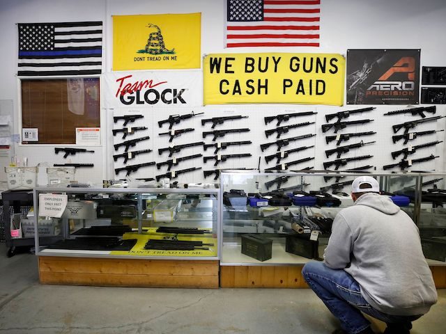 A customer looks at handguns in a case as AR-15 style rifles hang on a wall at Davidson De