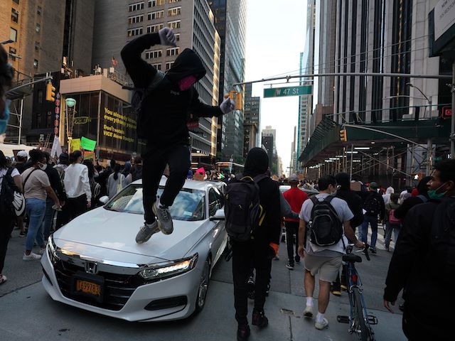A protester jumps on a car in midtown during demonstrations over the death of George Floyd by a Minneapolis police officer on June 1, 2020 in New York. - New York's mayor Bill de Blasio today declared a city curfew from 11:00 pm to 5:00 am, as sometimes violent anti-racism protests roil communities nationwide. Saying that "we support peaceful protest," De Blasio tweeted he had made the decision in consultation with the state's governor Andrew Cuomo, following the lead of many large US cities that instituted curfews in a bid to clamp down on violence and looting. (Photo by Bryan R. Smith / AFP) (Photo by BRYAN R. SMITH/AFP via Getty Images)
