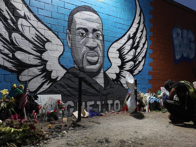 Joshua Broussard kneels in front of a memorial and mural that honors George Floyd at the S