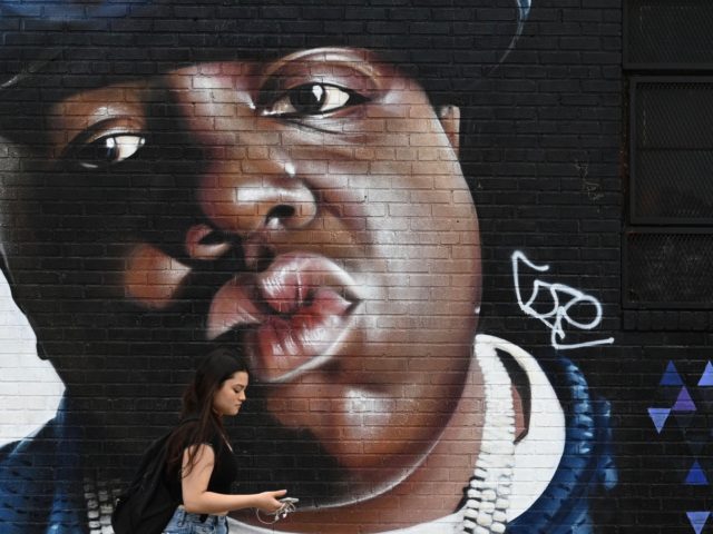 A woman passes by a mural by Brazilian artist Sipros of the rapper Biggie Smalls on a wall