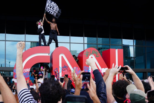 ATLANTA, GA - MAY 29: A man waves a Black Lives Matter flag atop the CNN logo during a protest in response to the police killing of George Floyd outside the CNN Center on May 29, 2020 in Atlanta, Georgia. Demonstrations are being held across the U.S. after George Floyd …