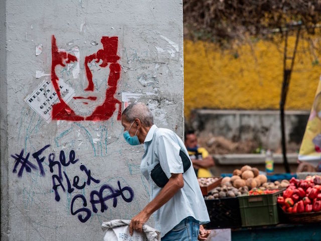 A man walks past a graffiti demanding Colombian businessman Alex Saab's freedom, in Caracas, on February 23, 2021. - Saab, who is allegedly close to Venezuelan President Nicolas Maduro and wanted in the US for money laundering, has been put under house arrest in Cape Verde. Saab was detained in June 2020 as a plane he was travelling on stopped over in the African country. (Photo by Yuri CORTEZ / AFP) (Photo by YURI CORTEZ/AFP via Getty Images)