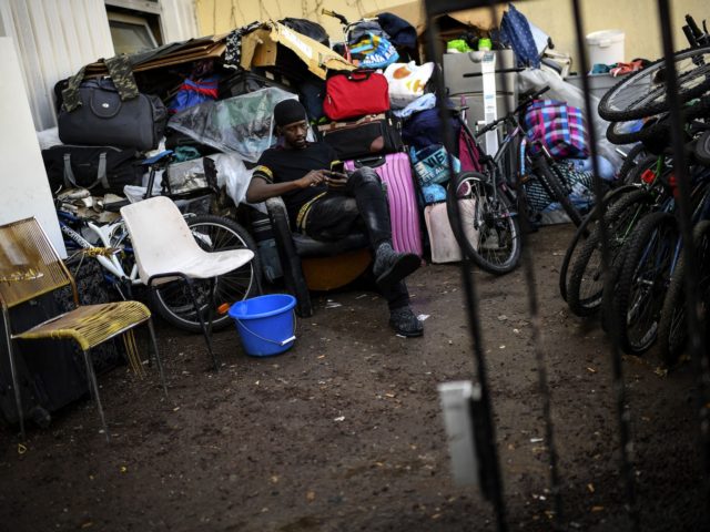 An African migrant checks his phone as he sits by piles of suitcases and bicycles outside