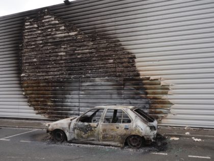 A picture taken on March 17, 2021 shows a burnt car in front of a damaged supermarket after a night of riots in the north of Blois, center France. - The clashes, which started with a refusal to obey, during a control by the Anti-Crime Brigade (Bac) in the northern …