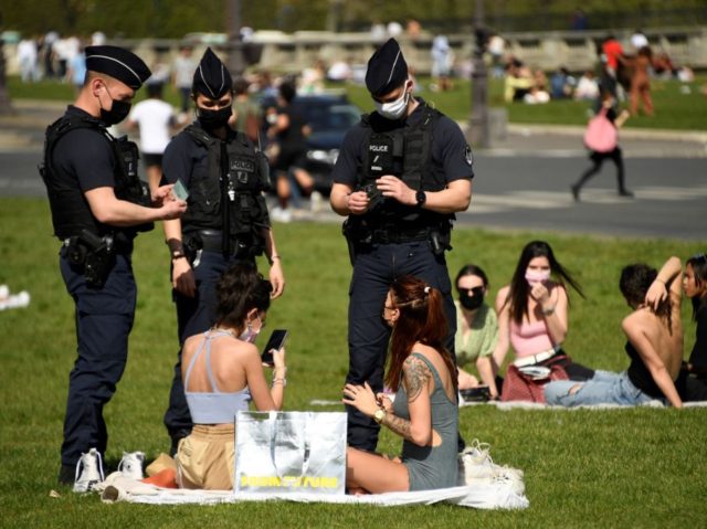 Police officers control people enjoying a sunny spring day on the grassin front of the Hot