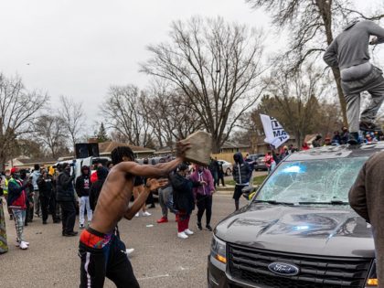 A man throws a rock at a police car as protesters clashwith the police after an officer shot and killed a black man in Brooklyn Center, Minneapolis, Minnesota on April 11,2021. - Protests broke out April 11, 2021 night after US police fatally shot a young Black man in a …