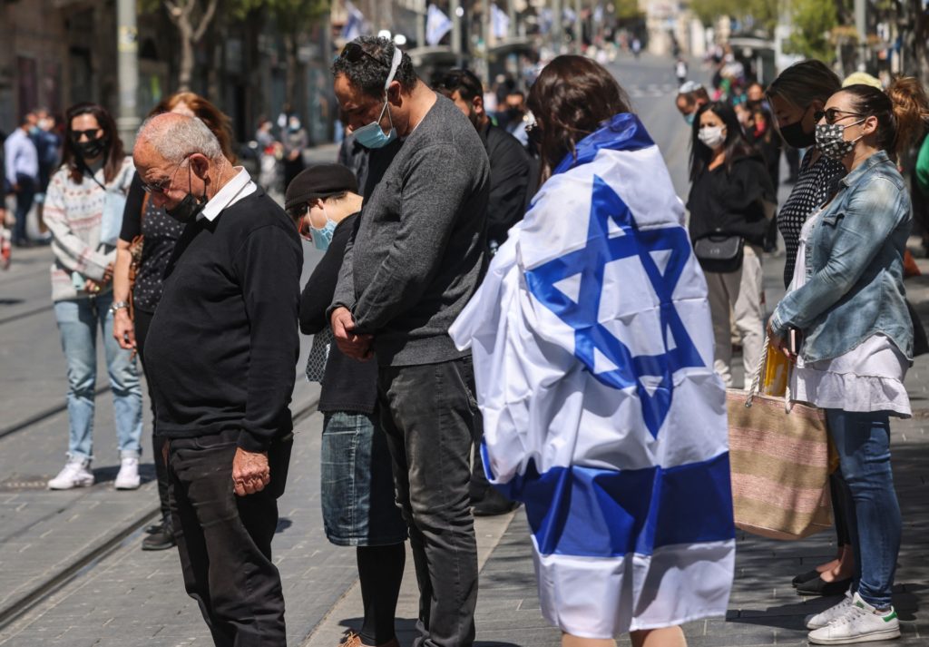 People stand still, some with Israeli flags, along Jaffa Street in the centre of Jerusalem as they observe a two-minute period of silence in tribute to fallen soldiers during Yom HaZikaron (Remembrance Day) on April 14, 2021. (Photo by Emmanuel DUNAND / AFP) (Photo by EMMANUEL DUNAND/AFP via Getty Images)