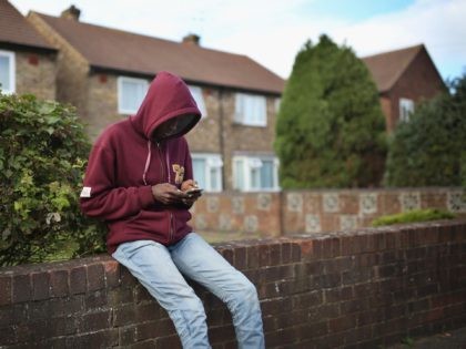 LONGFORD, ENGLAND - OCTOBER 14: A young asylum seeker checks his phone while sitting on a wall outside temporary housing on October 14, 2015 in Longford, England. Many Asylum seekers are currently being brought to the village to stay in temporary housing before being moved on which is, according to …
