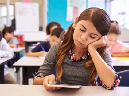 Bored girl reading tablet in elementary school class