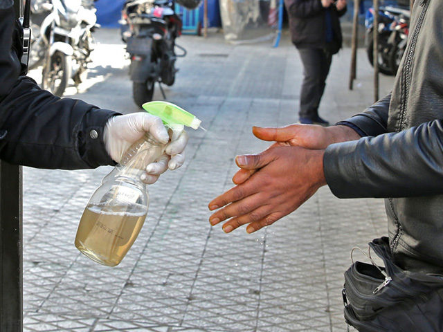 An Iranian man sprays alcohol on the hands of people outside an office building in Tehran on March 4, 2020. - Iran has scrambled to halt the rapid spread of the COVID-19 virus, shutting schools and universities, suspending major cultural and sporting events, and cutting back on work hours. (Photo …