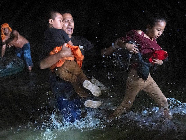 An immigrant father grips his children while walking ashore on the bank of the Rio Grande at the U.S.-Mexico border on April 14, 2021 in Roma, Texas. A smuggler (L), had rafted them over from Mexico with fellow immigrants. A surge of mostly Central American immigrants crossing into the United …