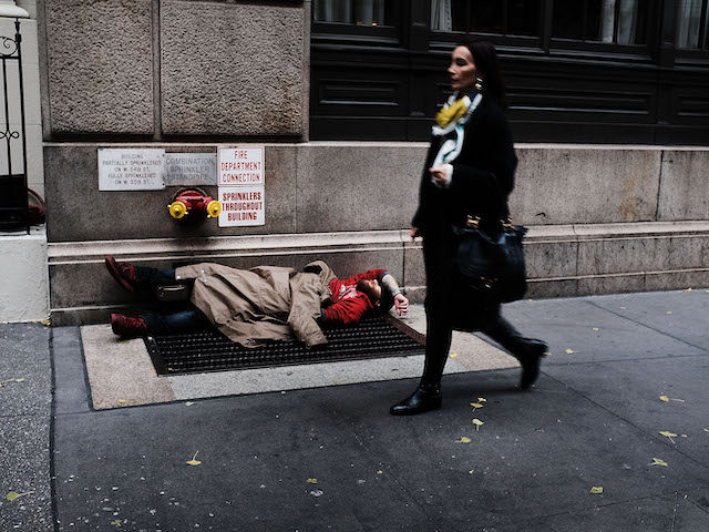 A woman walks by a homeless man along a Manhattan street on November 30, 2017 in New York