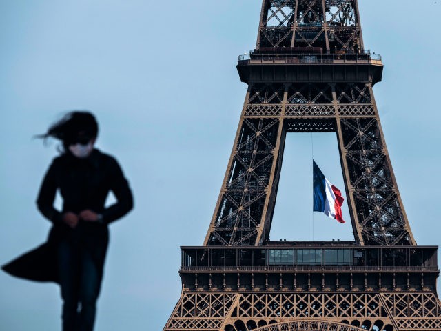 TOPSHOT - A woman wearing a face mask walks as a French national flag flies on the Eiffel Tower in background in Paris on May 11, 2020 on the first day of France's easing of lockdown measures in place for 55 days to curb the spread of the COVID-19 pandemic, …