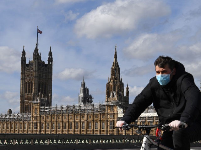 A man wearing a protective face mask cycles across Westminster Bridge, with the Houses of Parliament behind in central London on March 21, 2020, a day after the British government said it would help cover the wages of people hit by the coronavirus outbreak as it tightened restrictions to curb …