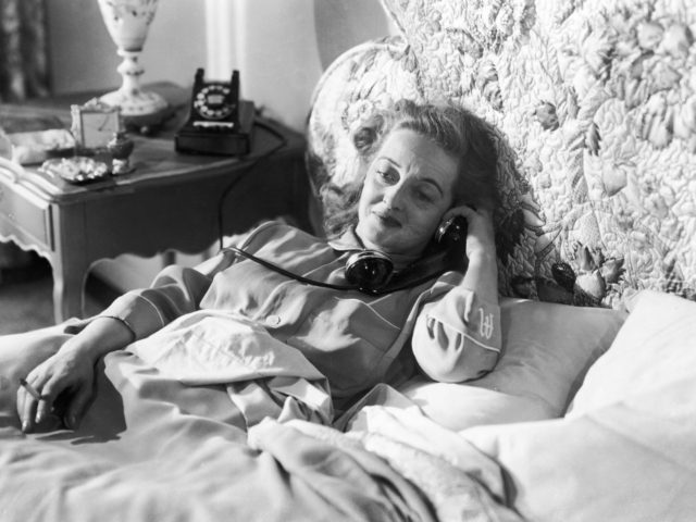 American actress Bette Davis (1908 - 1989) holds a telephone receiver whilst smoking a cigarette in bed in a still from the film 'All About Eve', directed by Joseph L. Mankiewicz, 1950. (Photo by 20th Century Fox/Archive Photos/Getty Images)