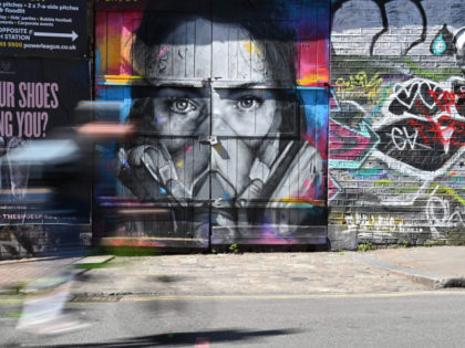 TOPSHOT - A cyclist passes a piece of graffiti of artist BK Foxx wearing her graffiti mask created by French street artist Zabou in East London on April 19, 2020, during the novel coronavirus COVID-19 pandemic. - The number of people in Britain who have died in hospital from coronavirus …