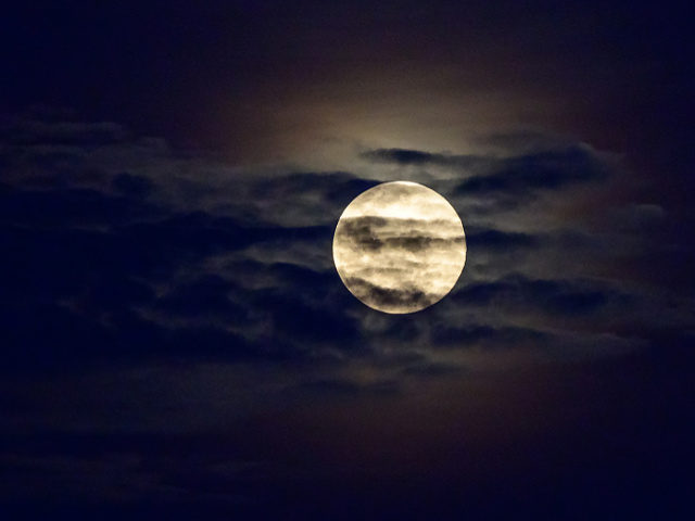 The full Worm Moon is seen behind the clouds in the sky over Bangkok on March 28, 2021. (P