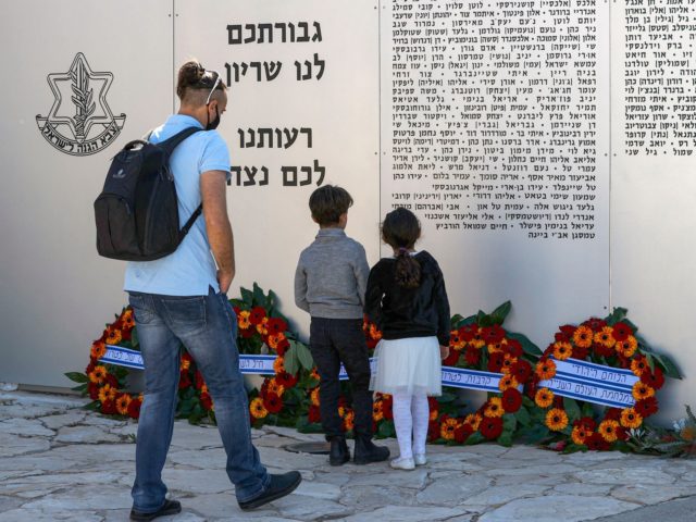 A man approaches children looking at names on a commemorative plaque honouring fallen Israeli soldiers at the Armoured Corps in Latrun, between Jerusalem and Tel Aviv, on April 14, 2021, following a ceremony commemorating Yom HaZikaron (Israel's Remembrance Day for fallen soldiers). - Israel annually marks Yom HaZikaron to commemorate …