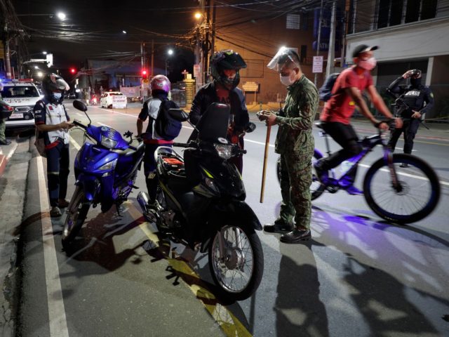Police inspect motorcycle riders at a checkpoint as curfew is imposed to prevent the spread of the coronavirus in metro Manila, Philippines a year after the country imposed a lockdown on Monday, March 15, 2021. The Department of Health has been reporting a surge in infections for more than a …