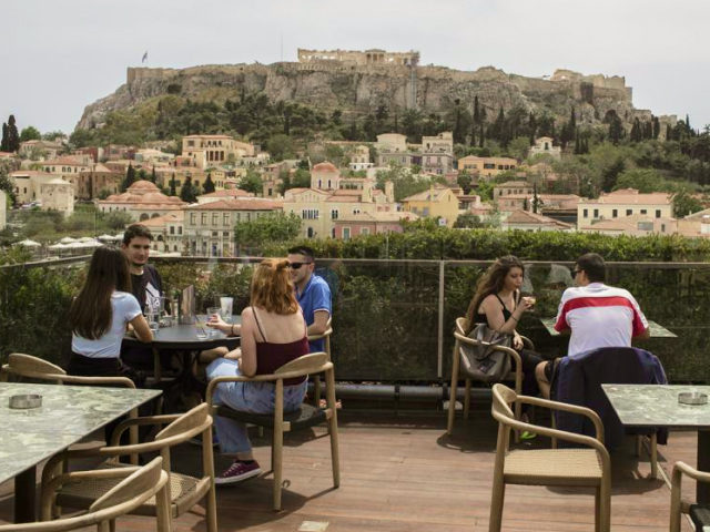 People sit in on a cafe terrace, in the Monastiraki district of Athens, with the ancient A