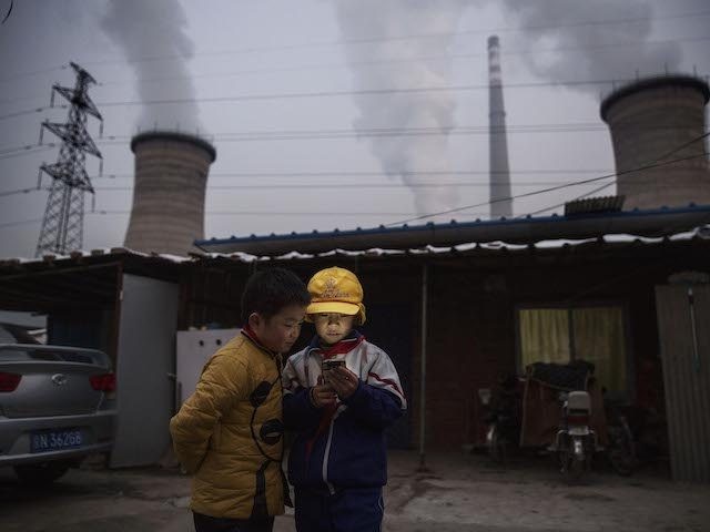 Chinese boys look at their smartphone in front of their house next to a coal fired power plant on November 27, 2015 on the outskirts of Beijing, China. China's government has set 2030 as a deadline for the country to reach its peak for emissions of carbon dioxide, what scientists …