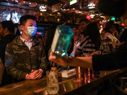 A man wearing a face mask as a preventive measure against the spread of the COVID-19 novel coronavirus, is seen while people dance in a bar in Shanghai on April 26, 2020. - China's economy shrank for the first time in decades last quarter as the coronavirus paralysed the country, …