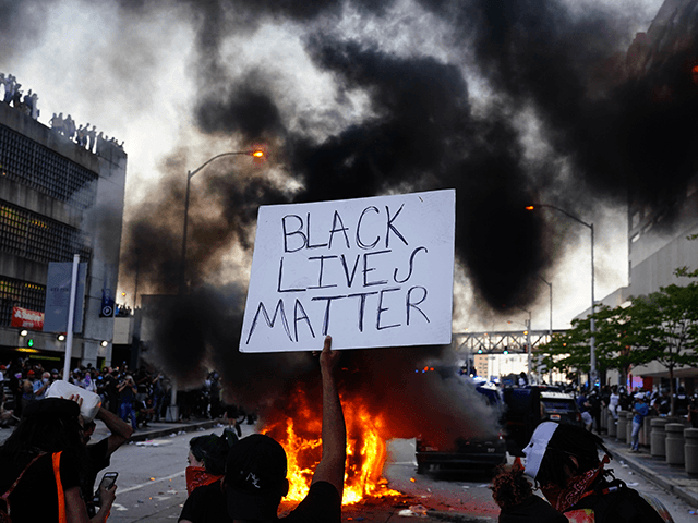A man holds a Black Lives Matter sign as a police car burns during a protest on May 29, 20