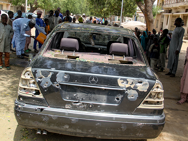 The wreckage of a car hit by an attack led by Boko Haram members is seen surrounded by residents of the Adam Kolo district of Maiduguri on February 24, 2021. - Boko Haram jihadists attacked the Nigerian city of Maiduguri in the volatile northeast, killing 16 people, including nine children …