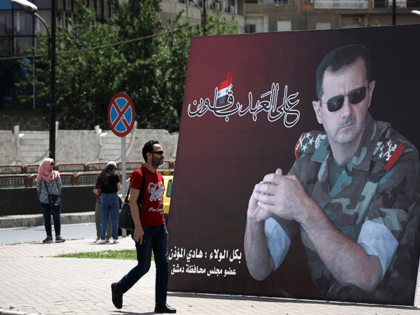 A Syrian man walks past a giant portrait of President Bashar al-Assad at the Umawiyin square in Syria's capital Damascus on May 3, 2021, ahead of this month's presidential elections. - A Syrian former minister and a member of the Damascus-tolerated opposition will face Bashar al-Assad in this month's presidential …