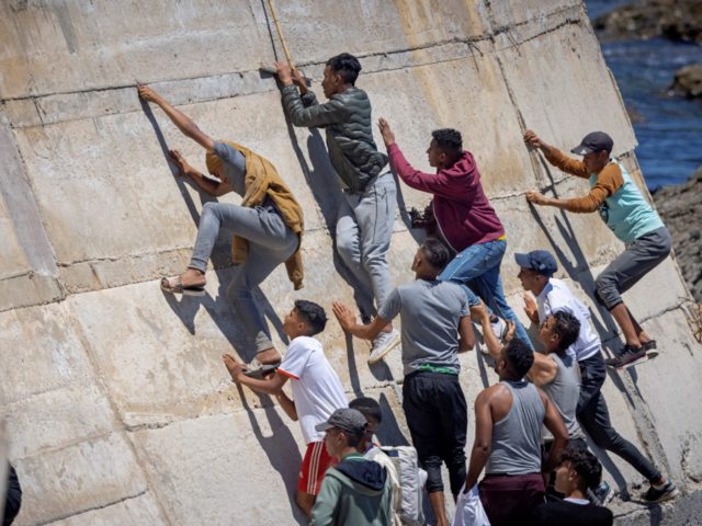 TOPSHOT - Migants climb a sea wall in the northern town of Fnideq after attempting to cross the border from Morocco to Spain's North African enclave of Ceuta on May 19, 2021. - Spain stepped up diplomatic pressure on Rabat as its prime minister flew into Ceuta, vowing to "restore …