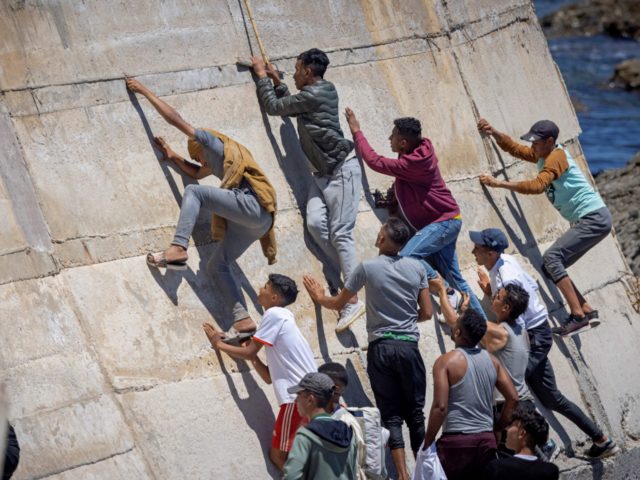 TOPSHOT - Migants climb a sea wall in the northern town of Fnideq after attempting to cros