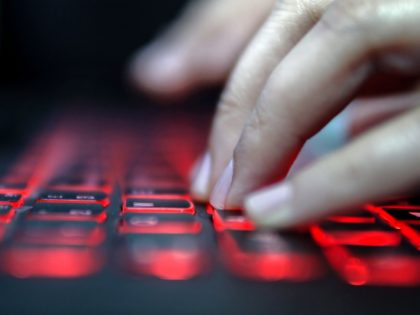 Teenage Hacker Girl Attacks Corporate Servers in Dark, Typing on Red Lit Laptop Keyboard. Room is Dark