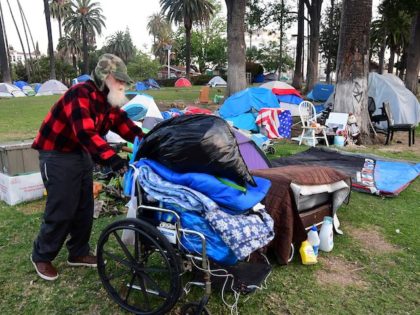 A homeless man pushes his belongings at a homeless encampment at Echo Park Lake where soci