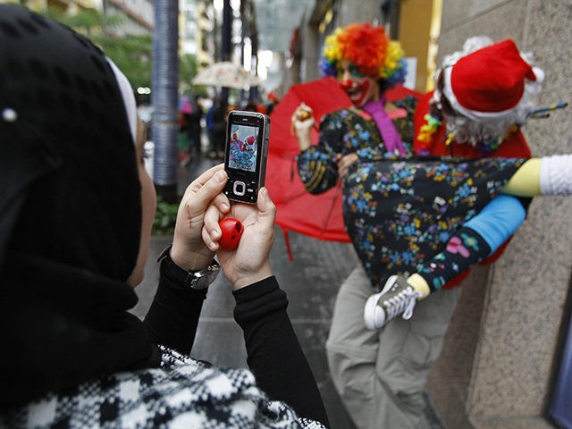 A Muslim woman takes a picture with her mobile of clowns and street performers in Beirut's