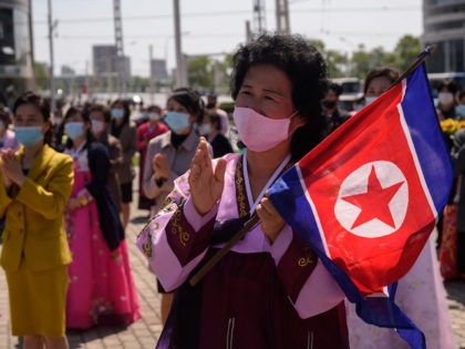 A woman wearing traditional dress and holding a North Korean flag watches a performance ce