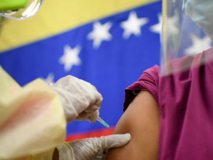 Backdropped by a national flag, a doctor inoculates a work colleague with a dose of the Russian COVID-19 vaccine Sputnik V at the Ana Francisca Perez de Leon II public hospital in Caracas, Venezuela, Friday, Feb. 19, 2021. (AP Photo/Matias Delacroix)