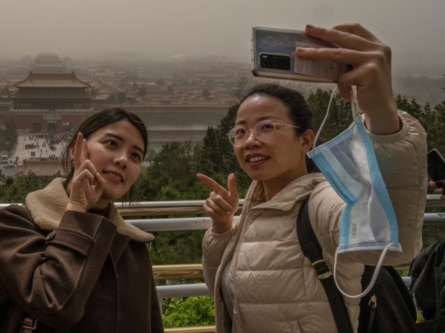BEIJING, CHINA - MARCH 28: Chinese tourists take their photo with the Forbidden City in the background from Jingshan Park during a sandstorm on March 28, 2021 in Beijing, China. China's capital and the northern part of the country was hit with a sandstorm Sunday, sending air quality indexes of …