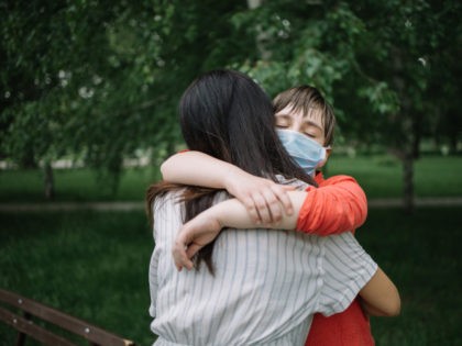 Portrait of mother and daughter cuddling in park during coronavirus pandemic - stock photo Portrait of mother and daughter cuddling in park during coronavirus pandemic. Young girl with protection mask embracing woman outdoor.