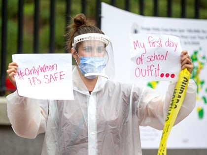 BOSTON, MA - AUGUST 19: A woman in personal protective equipment (PPE) holds up signs at a standout protest organized by the American Federation of Teachers at the Massachusetts State House on August 19, 2020 in Boston, Massachusetts. The group is calling for a uniform requirement for all districts to …