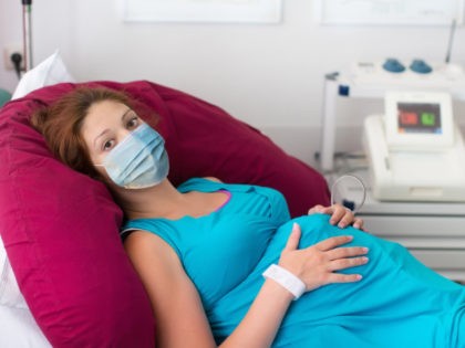 Pregnant woman in clinic wearing face mask - stock photo Pregnant patient in face mask in a hospital at doctor visit during coronavirus outbreak. Mother giving birth to baby in covid-19 lockdown. Pregnancy examination. Expecting woman in labor and delivery.