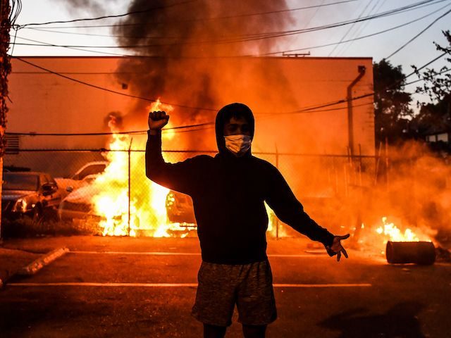 TOPSHOT - A protestor gestures as cars burn behind him during a demonstration in Minneapolis, Minnesota, on May 29, 2020 over the death of George Floyd, a black man who died after a white policeman kneeled on his neck for several minutes. - The Minneapolis police officer accused of killing …