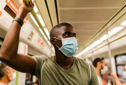 Young man wearing mask looking away while standing in subway train - stock photo
