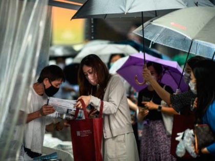 People hold umbrellas as a newsstand vendor (L) helps a customer protect her copy of the Apple Daily newspaper's final issue from the rain after she queued up to buy it from the street stall in Hong Kong on June 24, 2021, after Apple Daily was forced to close under …