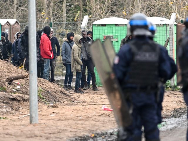 Police stand next to migrants at the makeshift camp in Calais, northern France, on Novembe