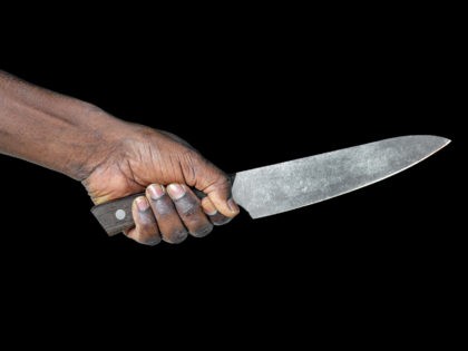 African man hold knife - aggression. Big kitchen knife in man hand. Large kitchen knife in a man's hand. Hand of african man holding a knife isolated on a black background.
