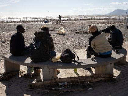 A group of migrants sit by the shore in Ventimiglia on October 3, 2020 after the Roya river flooded overnight, submerging the whole city with water and mud. - One person died and authorities listed some 20 as missing after heavy storms lashed southern France and northern Italy with hundreds …