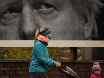 A woman wearing a protective face mask passes a billboard showing Britain's Prime Minister